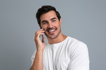 Handsome young man talking on smartphone against grey background