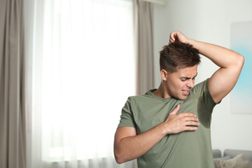 Young man with sweat stain on his clothes indoors, space for text. Using deodorant