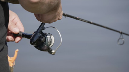 Male hand holding fishing rod and reeling the other hand