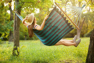 Young woman swinging in comfortable hammock at green garden