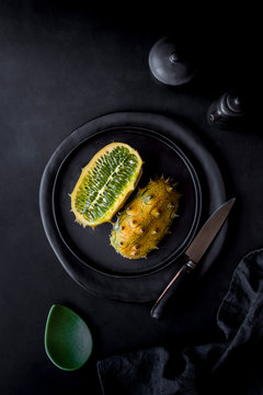 Overhead view of halved kiwano - horned melon on black plate