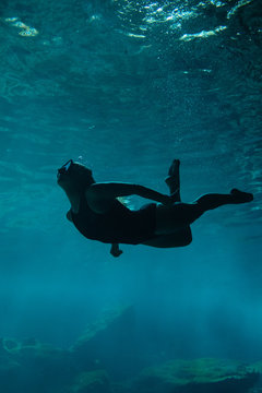 A young women swimming beneath the surface of clear blue water in a cenote in Mexico.