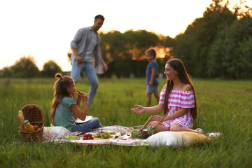 Happy family having picnic in park at sunset