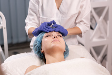 Cosmetologist in blue gloves does facial massage. Woman enjoys the procedure. Anti-aging massage. Cosmetic procedures