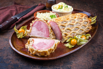 Backed Kasseler saddle of pork steak with sauerkraut and potato salad as closeup offered on a plate with physalis fruit