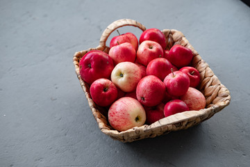 Red apples in a wicker basket stand on a gray background. Fresh Autumn Harvest