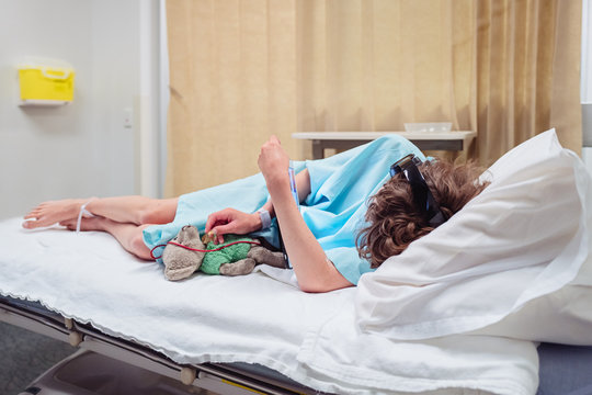 Child in a hospital bed with a hospital gown and teddy bear