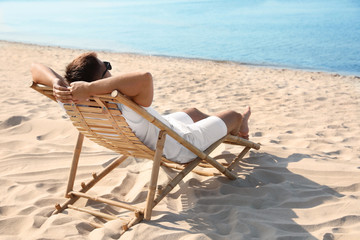 Young man relaxing in deck chair on sandy beach