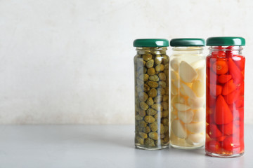 Jars with pickled vegetables on grey table against light background. Space for text