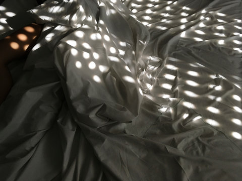 Unrecognizable lady sleeping in bed covered by window shadow.