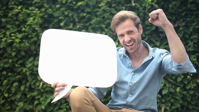 excited young casual man celebrates succeess while showing blank speech bubble