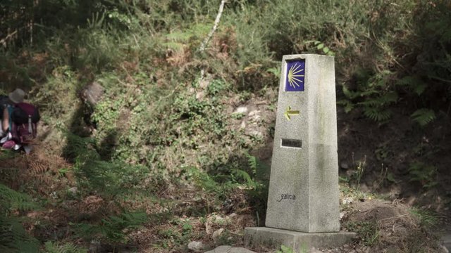 Way of St. James sign and pilgrims walking on a forest footpath. Yellow scallop sign pilgrimage to Santiago de Compostela