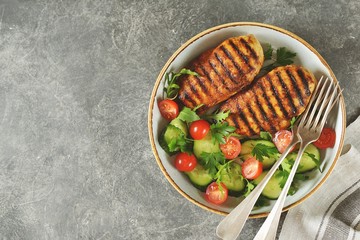 Grilled healthy chicken breast with a salad of cherry tomatoes, cucumbers, arugula and parsley.