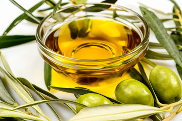 Olive oil. Greek olive oil in glass transparent bowl with olive branches with leaves and olives. Close-up on white surface.