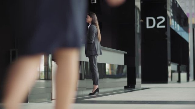 Lockdown wide shot of beautiful young businesswoman receiving document at secretary counter in modern office building and walking away. Middle aged woman passing by