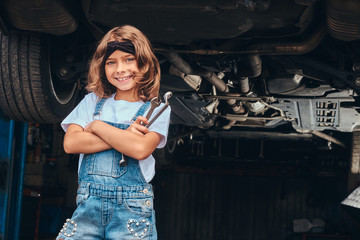 Pretty cheerful girl is holding wrenches in hangs while posing for photographer at auto service.