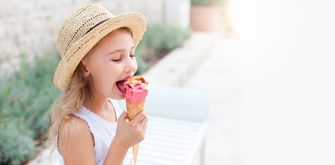 Kid is eating ice cream. Happy Little girl is enjoying italian gelato in town. Cute child in straw hat is tasting delicious street food in summer travel outdoors. Light background, free space for text - obrazy, fototapety, plakaty