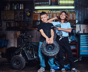 Fototapeta na wymiar Dream team in action - two kids are having fun while posing for photographer at auto workshop.