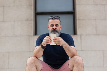 Bearded man sitting outside, in shorts and blue t-shirt, checking his phone
