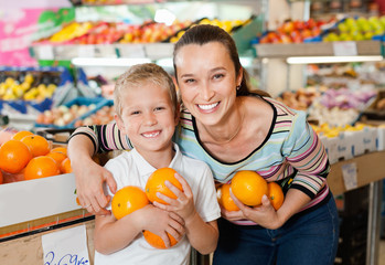 Fototapeta premium Portrait of happy woman and her little son choosing oranges at shop