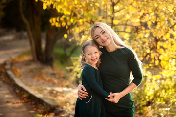 happy lovely mother and daughter for 3-4 years in identical green dresses in autumn in nature in the park, my mother has long blond hair, her daughter has wonderful curls, family walk