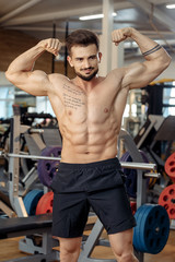 Fototapeta na wymiar Handsome muscular athletic young man bodybuilder fitness model show his biceps after exercises in gym.