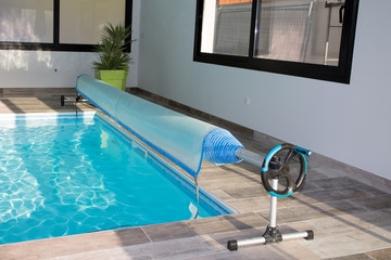 Pool cover rolled on edge of blue swimming pool during the summer