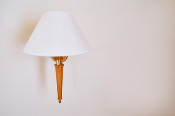 Wall lamp with white cone shade, copy space. Part of the interior in the hotel room, background. Lamp with a wooden stem attached to a beige wall.
