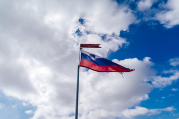 Slovenia flag on top of Kriska Gora mountain. National flag of alpine state Slovenia, blue sky, white clouds. Flag in wind.