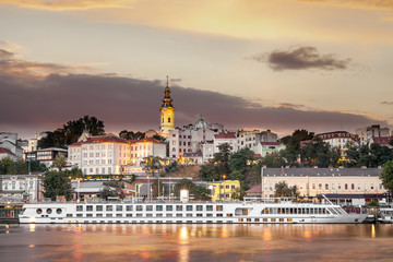 Golden hour view of Belgrade riverfront with Sava river in the foreground, holy archangel Michael cathedral at the back and impressive, large cruiser ship in the harbor