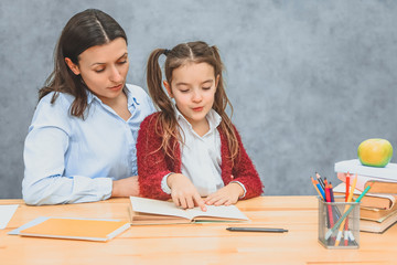 Mother and daughter read a book on a gray background, doing homework. Dressed in beautiful shirts.