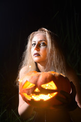 Beautiful young woman with pumpkin jack in hands on Halloween. Bright luminous sinister pumpkin as a symbol of Halloween. The concept of a festive party.