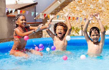 Fototapeta na wymiar Three laughing and screaming kids play in the pool