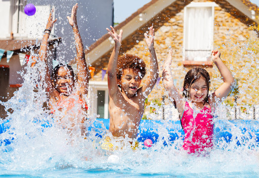 Portrait of three kids splash water in garden pool