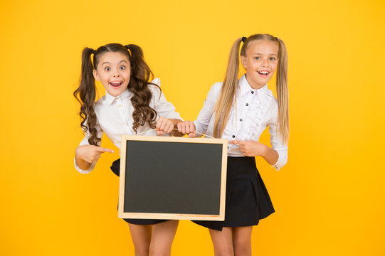 Lesson ideas. Happy small schoolchildren pointing at lesson plan on blackboard on yellow background. Little girls having lesson in primary school. Recording a lesson using blackboard, copy space