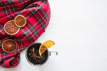 Christmas mulled red wine with dried oranges on a wooden white table. Traditional hot drink at winter. Tartan pattern fabric plaid. Copy space. 