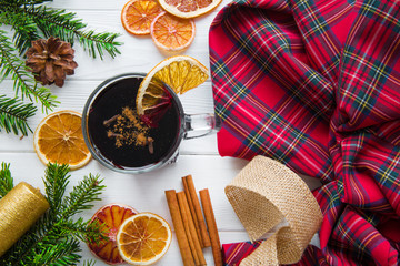 A cup of hot winter beverage mulled wine with oranges and cinnamon sticks, christmas check pattern...
