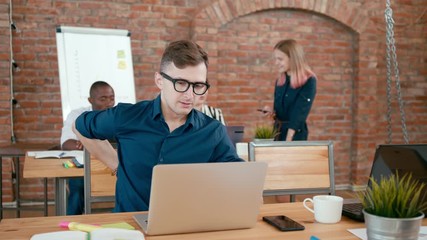 Tired Male Caucasian Startup Worker has Backache, Suffering from Pain in Back and Neck after Working on Laptop in Loft Office. 4K Static Medium Shot