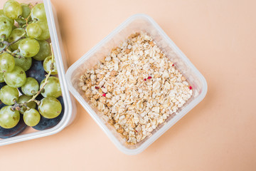 the right breakfast of green and black grapes and cereal muesli. granola and fresh fruits in a lunchbox on a pastel beige background.