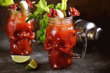 Bloody Mary cocktail in glass skull with celery sticks, pink salt, lime and canapes from canned vegetables. Halloween drink. 