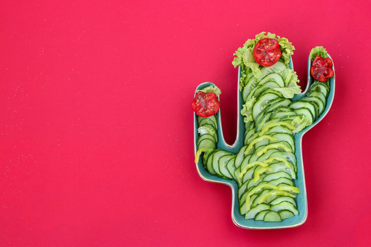 Cucumber, pepper and tomato salad in a ceramic plate in the shape of a cactus on a red background, horizontal orientation, copy space