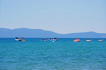 Fototapeta na wymiar Panoramic view of lake Tahoe under a blue summer sky with some boats anchored and a mountain range in the distant background