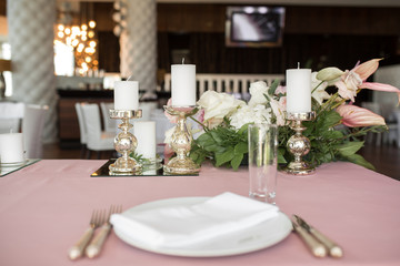 The wedding table setting for the newlyweds is decorated with fresh flowers of carnation, rose, anthurium and eucalyptus leaves. Silver candlesticks, white candles. Wedding floristry. Closeup details
