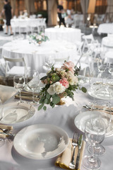 Wedding table setting decorated with fresh flowers in a brass vase. Wedding floristry. Banquet table for guests outdoors with a view of green nature. Bouquet with roses, eustoma and eucalyptus leaves