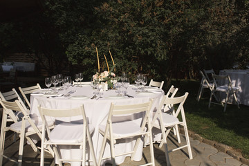 Wedding table setting decorated with fresh flowers in a brass vase. Wedding floristry. Banquet table for guests outdoors with a view of green nature. Bouquet with roses, eustoma and eucalyptus leaves