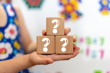 Questions child education concept on wooden cubes in little girl hands.