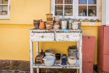 An old sideboard with pots standing on the paved sidewalk, against a yellow wall