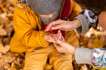 Fototapeta na wymiar A little boy in an autumn park sits on yellow leaves in a yellow jacket and holds a ladybug in children's hands. A red beetle crawls on the fingers of a child.