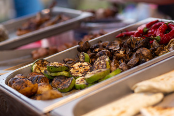 A counter with metal trays containing grilled food. Food and cooking equipment at a street food festival