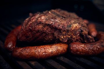 cooked beef, served on a white plate and a table with sausage companions